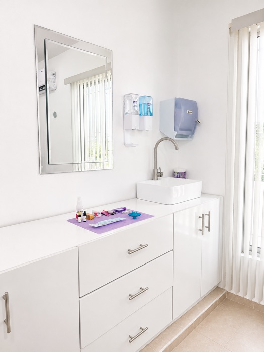 Zona de lavado e higiene con lavabo, mobiliario blanco e instrumental ordenado